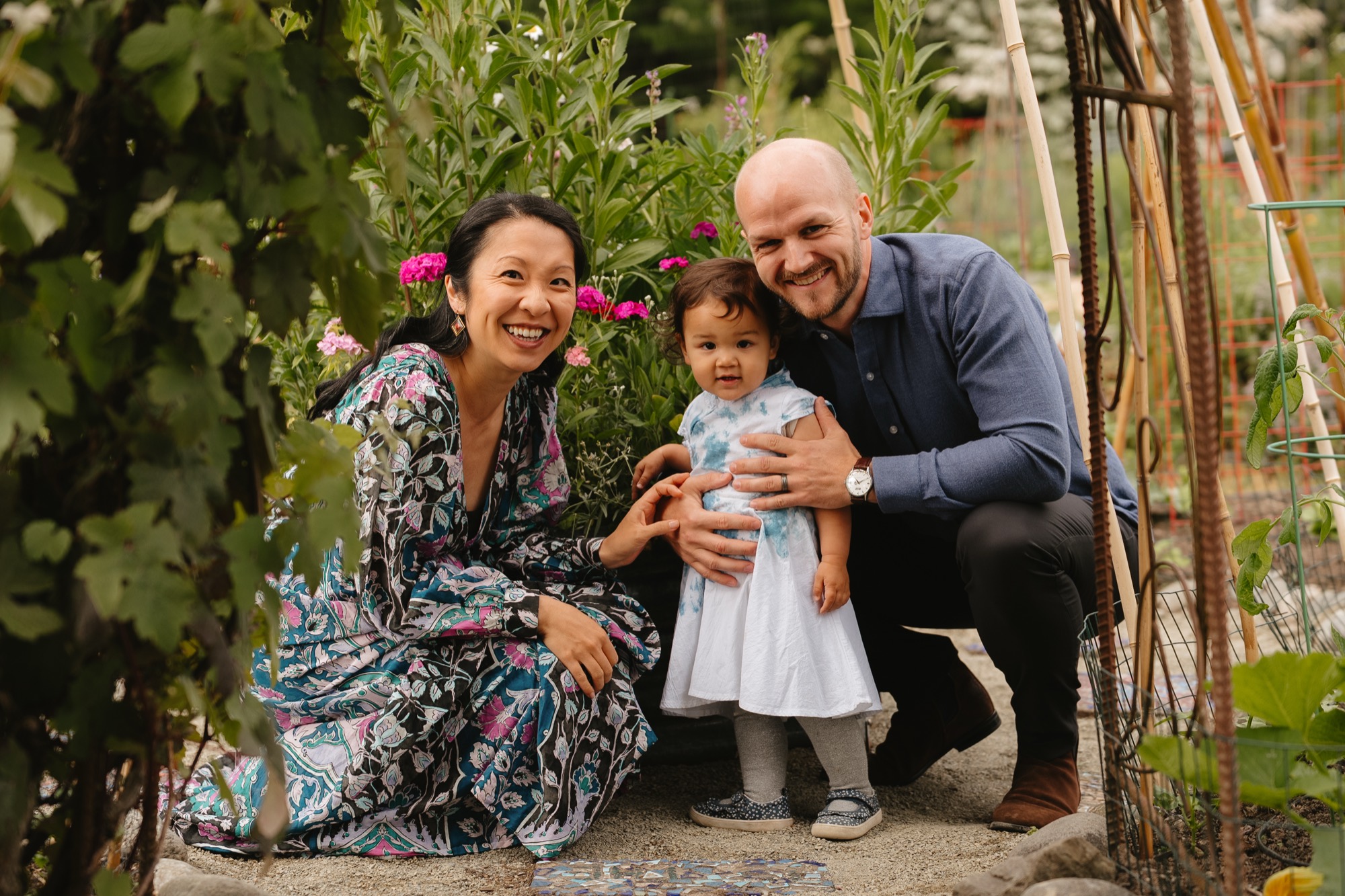 Serene and Mikkel crouched together with Lana among tall garden flowers